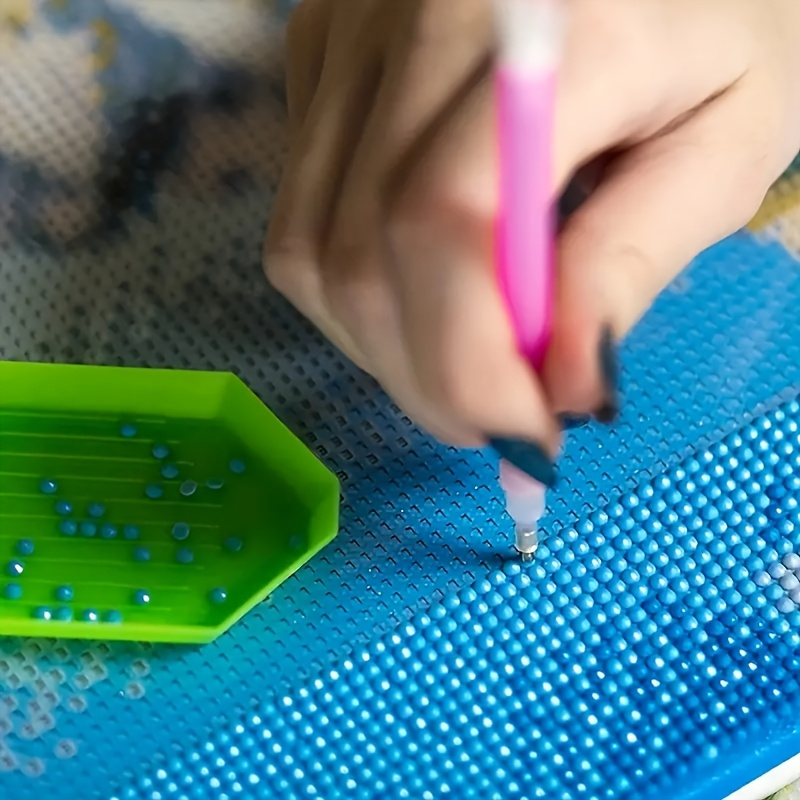 Person working on a craft project with beads and a tool on a blue mat.
