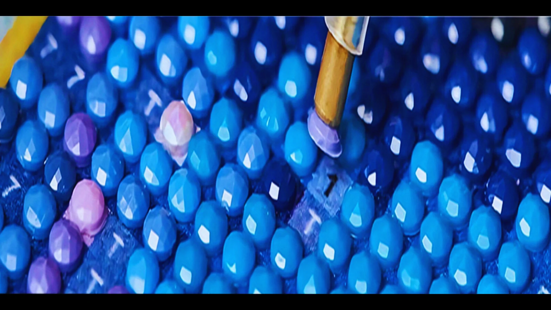Close-up of blue and purple beads with a needle penetrating one bead.
